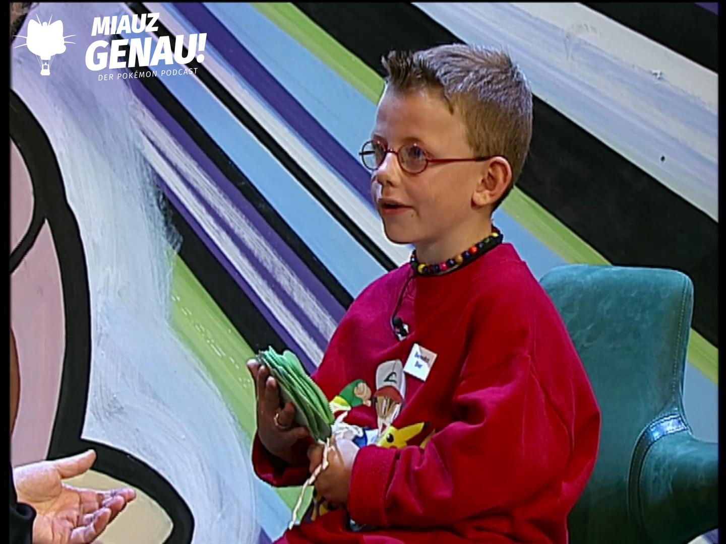 Benedict Bier im roten Pokémon-Pullover bei Wetten, dass..? mit seinem grünen Glücksbringer in den Händen.